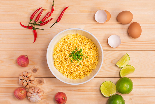 Instant noodles in bowl with vegetables on wood background