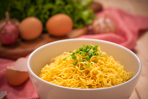 Instant noodles in bowl with vegetables on wood background