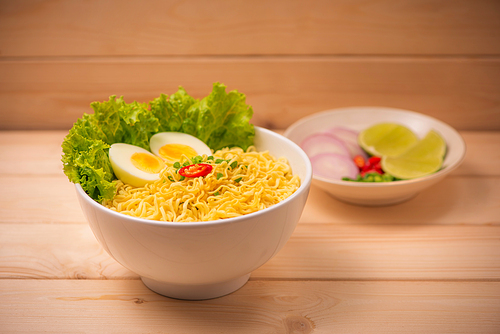 Instant noodles in bowl with vegetables and  boiled egg on wood background