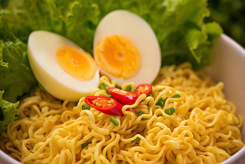 Instant noodles in bowl with vegetables and  boiled egg on wood background