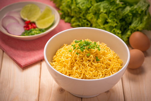 Instant noodles in bowl with vegetables on wood background