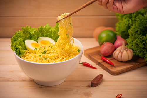 Instant noodles in bowl with vegetables and  boiled egg on wood background