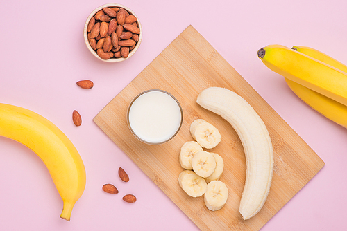 Bananas with almonds and milk on pink background.