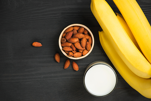 A banch of bananas with almonds and milk on wooden background.