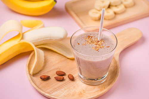 Fresh made banana smoothie in a glass on pink background