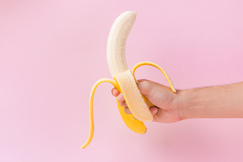 Male hand holding peeled banana isolated on pink background.
