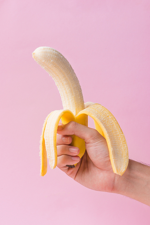 Male hand holding peeled banana isolated on pink background.