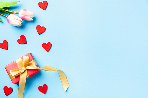 Happy Valentines' day background concept. Red gift box with a golden bow ribbon and wood red hearts composition greeting card for love isolated on blue background with copy space. Top View from above