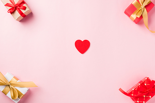 Valentines' day background. Frame made of red gift box with ribbon bow and wood red hearts shaped composition greeting card for love isolated on pink background with copy space. Top View from above