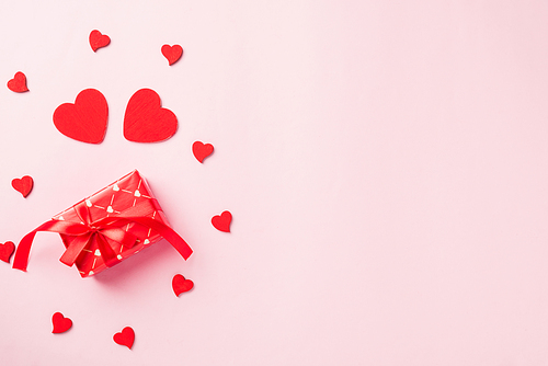 Valentines' day background. Red gift box with ribbon bow and wood red hearts shaped composition greeting card for love isolated on pink background with copy space. Top View from above