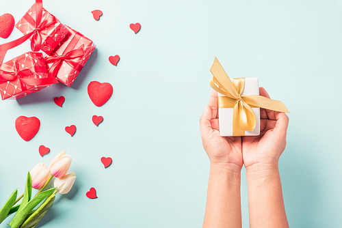 Valentine's day and birthday. Woman hands holding gift or present box decorated and red heart surprise on blue background, Female's hand hold gift box package in craft paper Top view flat lay