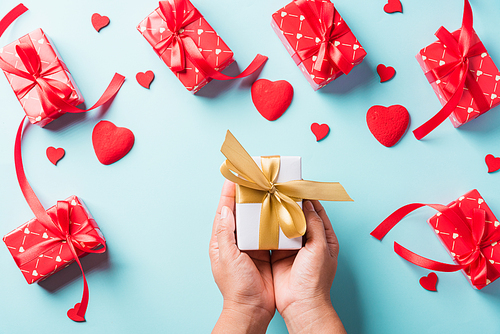 Valentine's day and birthday. Woman hands holding gift or present box decorated and red heart surprise on blue background, Female's hand hold gift box package in craft paper Top view flat lay