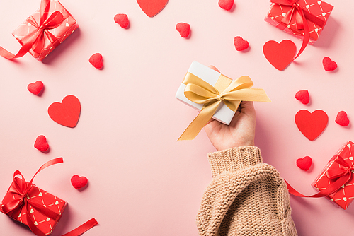 Valentine's day and birthday. Woman hands holding gift or present box decorated and red heart surprise on pink background, Female's hand hold gift box package in craft paper Top view flat lay