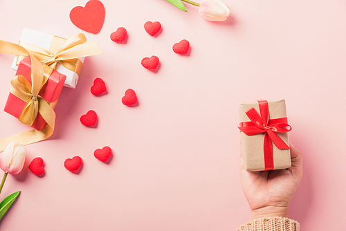 Valentine's day and birthday. Woman hands holding gift or present box decorated and red heart surprise on pink background, Female's hand hold gift box package in craft paper Top view flat lay