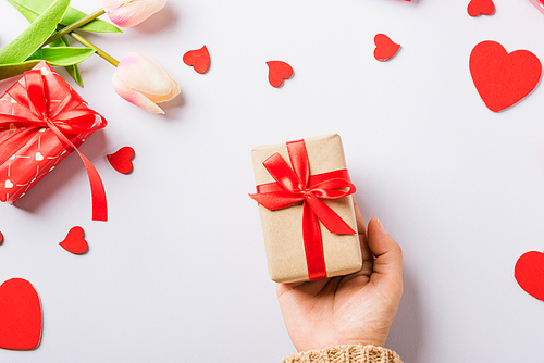 Valentine's day and birthday. Woman hands holding gift or present box decorated and red heart surprise on white background, Female's hand hold gift box package in craft paper Top view flat lay