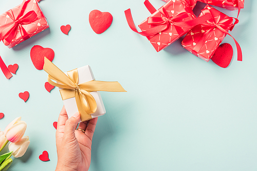 Valentine's day and birthday. Woman hands holding gift or present box decorated and red heart surprise on blue background, Female's hand hold gift box package in craft paper Top view flat lay