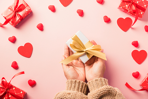 Valentine's day and birthday. Woman hands holding gift or present box decorated and red heart surprise on pink background, Female's hand hold gift box package in craft paper Top view flat lay