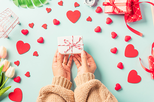 Valentine's day and birthday. Woman hands holding gift or present box decorated and red heart surprise on blue background, Female's hand hold gift box package in craft paper Top view flat lay