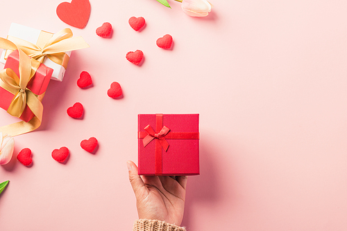 Valentine's day and birthday. Woman hands holding gift or present box decorated and red heart surprise on pink background, Female's hand hold gift box package in craft paper Top view flat lay