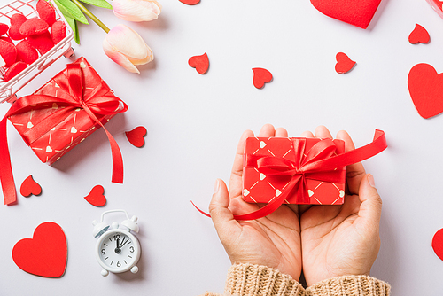 Valentine's day and birthday. Woman hands holding gift or present box decorated and red heart surprise on white background, Female's hand hold gift box package in craft paper Top view flat lay