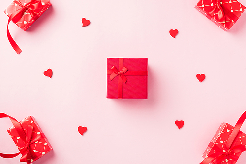 Valentines' day background. Red gift box with ribbon bow and wood red hearts shaped composition greeting card for love isolated on pink background with copy space. Top View from above