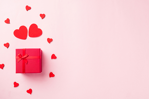 Valentines' day background. Red gift box with ribbon bow and wood red hearts shaped composition greeting card for love isolated on pink background with copy space. Top View from above