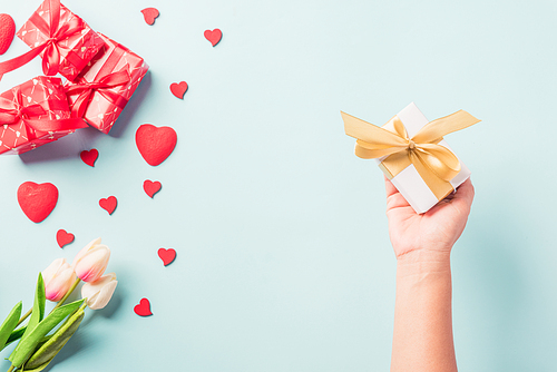 Valentine's day and birthday. Woman hands holding gift or present box decorated and red heart surprise on blue background, Female's hand hold gift box package in craft paper Top view flat lay