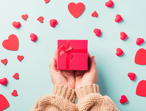 Valentine's day and birthday. Woman hands holding gift or present box decorated and red heart surprise on blue background, Female's hand hold gift box package in craft paper Top view flat lay