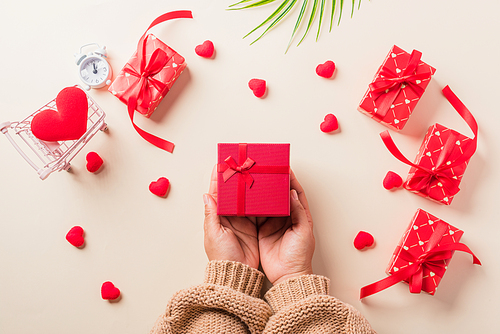 Valentine's day and birthday. Woman hands holding gift or present box decorated and red heart surprise on cream pastel background, Female's hand hold gift box package in craft paper Top view flat lay