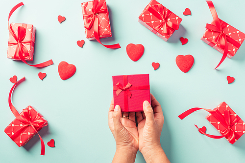 Valentine's day and birthday. Woman hands holding gift or present box decorated and red heart surprise on blue background, Female's hand hold gift box package in craft paper Top view flat lay