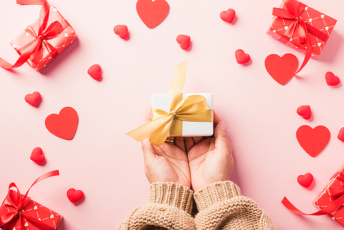 Valentine's day and birthday. Woman hands holding gift or present box decorated and red heart surprise on pink background, Female's hand hold gift box package in craft paper Top view flat lay