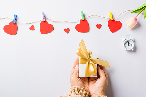 Valentine's day and birthday. Woman hands holding gift or present box decorated and red heart surprise on white background, Female's hand hold gift box package in craft paper Top view flat lay