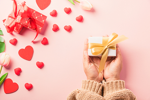 Valentine's day and birthday. Woman hands holding gift or present box decorated and red heart surprise on pink background, Female's hand hold gift box package in craft paper Top view flat lay