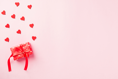 Valentines' day background. Red gift box with ribbon bow and wood red hearts shaped composition greeting card for love isolated on pink background with copy space. Top View from above