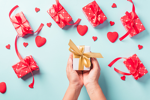 Valentine's day and birthday. Woman hands holding gift or present box decorated and red heart surprise on blue background, Female's hand hold gift box package in craft paper Top view flat lay