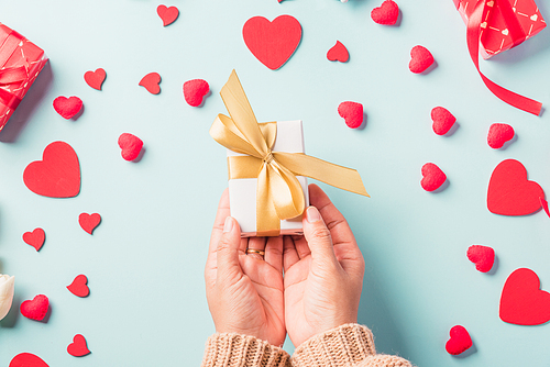 Valentine's day and birthday. Woman hands holding gift or present box decorated and red heart surprise on blue background, Female's hand hold gift box package in craft paper Top view flat lay