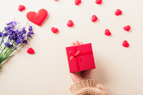 Valentine's day and birthday. Woman hands holding gift or present box decorated and red heart surprise on cream pastel background, Female's hand hold gift box package in craft paper Top view flat lay