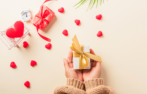 Valentine's day and birthday. Woman hands holding gift or present box decorated and red heart surprise on cream pastel background, Female's hand hold gift box package in craft paper Top view flat lay