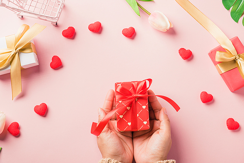 Valentine's day and birthday. Woman hands holding gift or present box decorated and red heart surprise on pink background, Female's hand hold gift box package in craft paper Top view flat lay