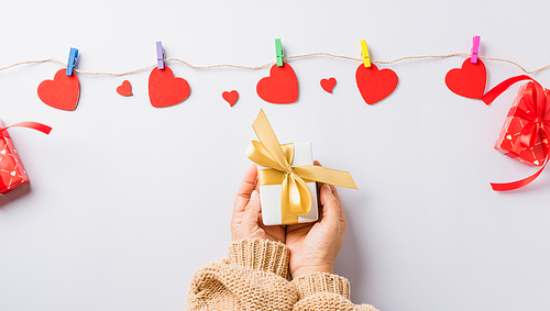 Valentine's day and birthday. Woman hands holding gift or present box decorated and red heart surprise on white background, Female's hand hold gift box package in craft paper Top view flat lay