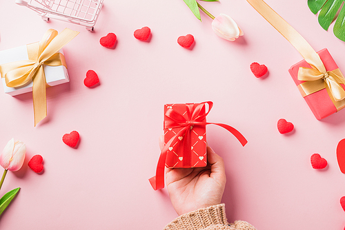 Valentine's day and birthday. Woman hands holding gift or present box decorated and red heart surprise on pink background, Female's hand hold gift box package in craft paper Top view flat lay