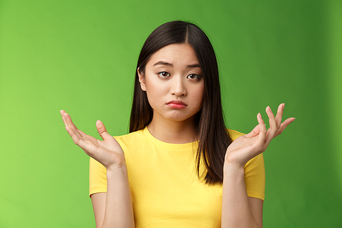 Close-up confused unemotive brunette woman spread hands sideways full dibelief, questioned what happening, look apathy reluctant, stand green background frustrated, no emotions. Copy space