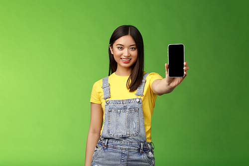 Self-assured attractive asian brunette show smartphone screen, introduce new telephone appllication, beating score cellphone game, smiling delighted, give recommendation follow own blog.