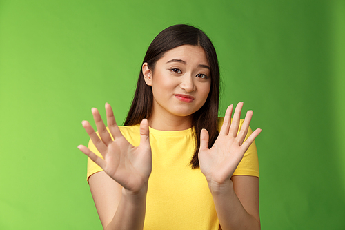 Modest cute insecure timid asian girl waving hands no gesture, step back, smirk, cringe aversion and dislike, refusing suspiciosu offer, rejecting proposal, stand green background. Copy space