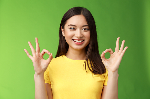 Everything under control. Friendly pleasant relaxed asian girl keep calm, assure all good, show okay ok sign, smiling approval, accept excellent idea, stand green background upbeat delighted quality.