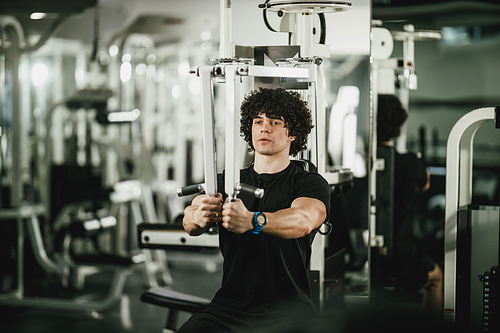 A young muscular man is doing training on machine in the gym.