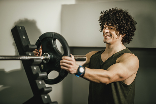 A muscular guy working out at the gym. He is putting more weights plate on barbell before the start exercising.