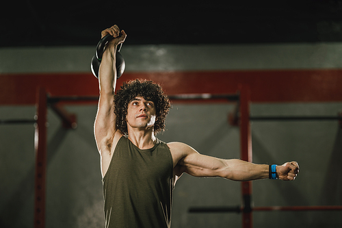 A young muscular man is doing hard training with kettlebell at the gym.