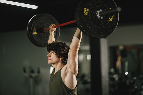 A young muscular man is doing hard training with barbell at the gym.