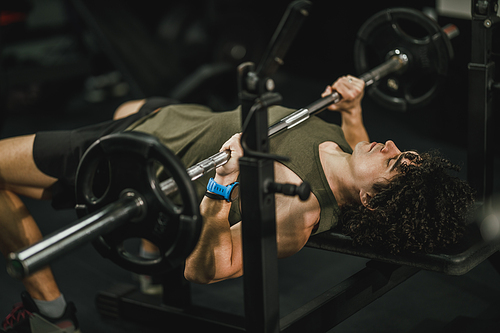 Shot of a muscular guy working out at the hard training in the gym. He is pumping up chest muscle with heavy weight.